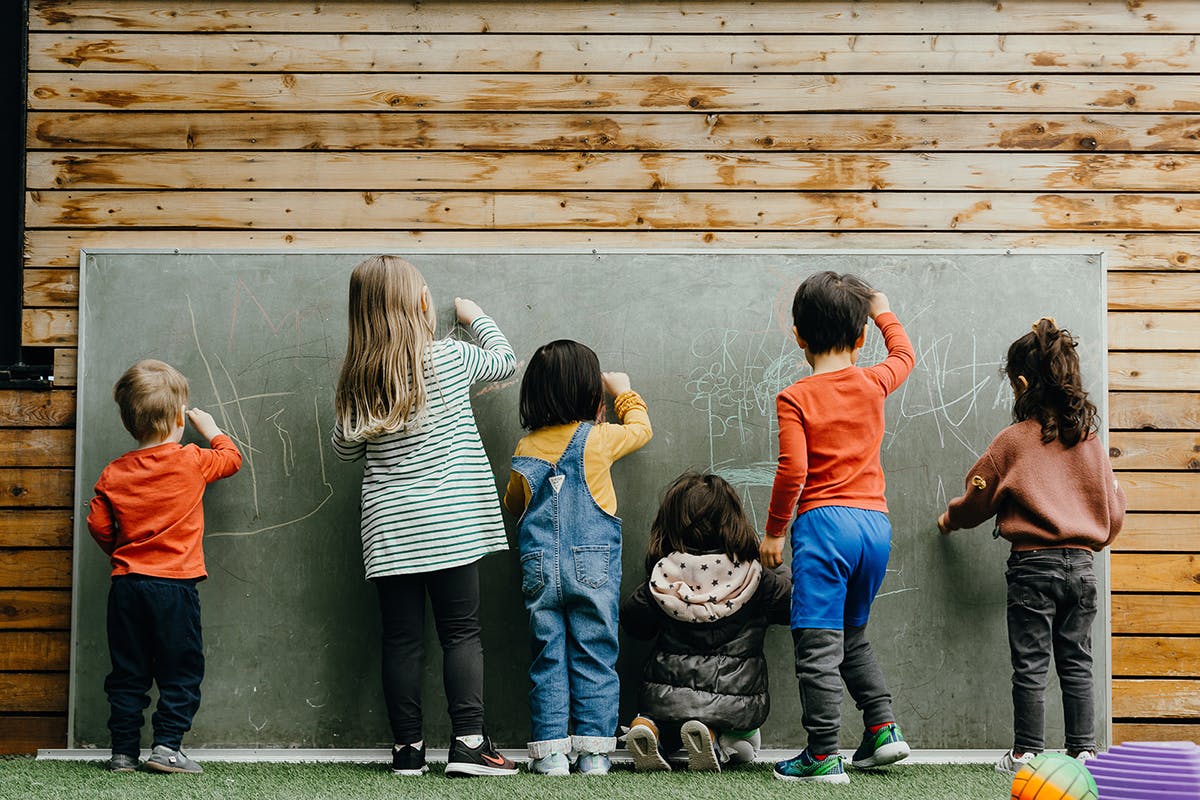 Children drawing on a large chalkboard outdoors