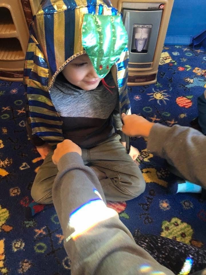 Child in a costume with a snake headpiece, with hands reaching towards them