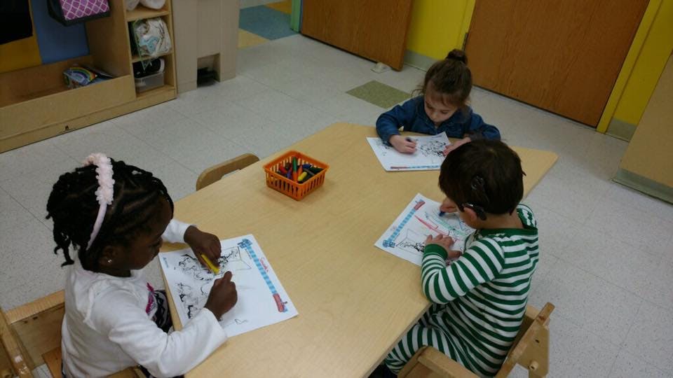 Three children drawing at a table in a classroom