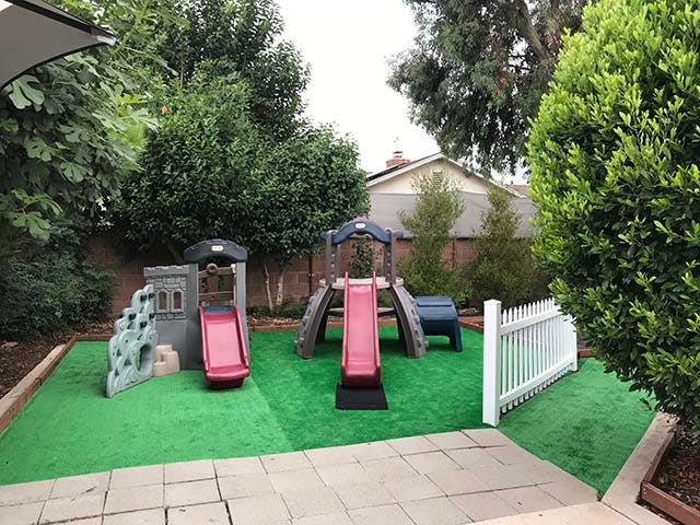 Two red slides and play structures on artificial grass
