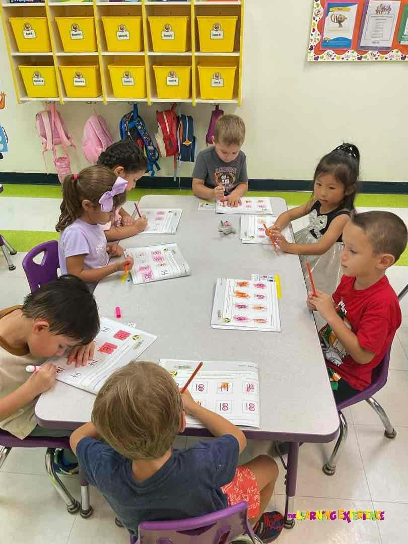 Children sitting at a table in a classroom working on worksheets