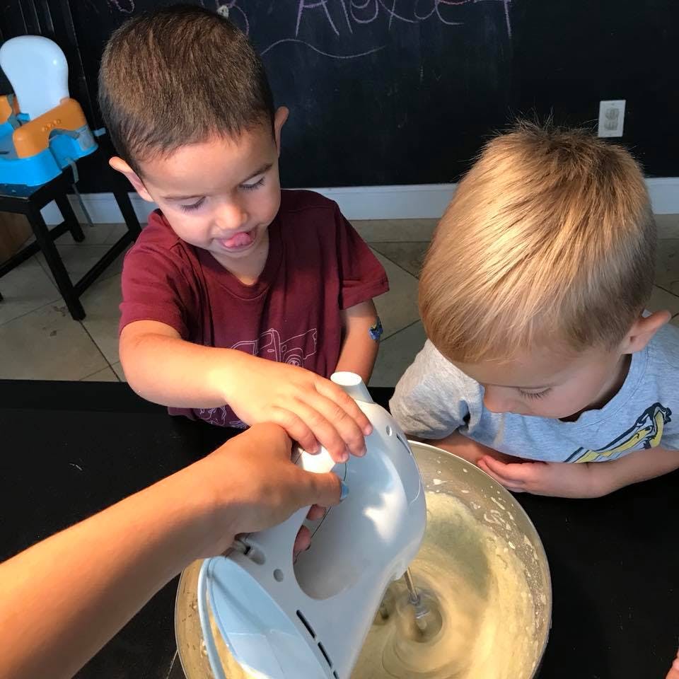 Two children watching a person use a hand mixer in a bowl