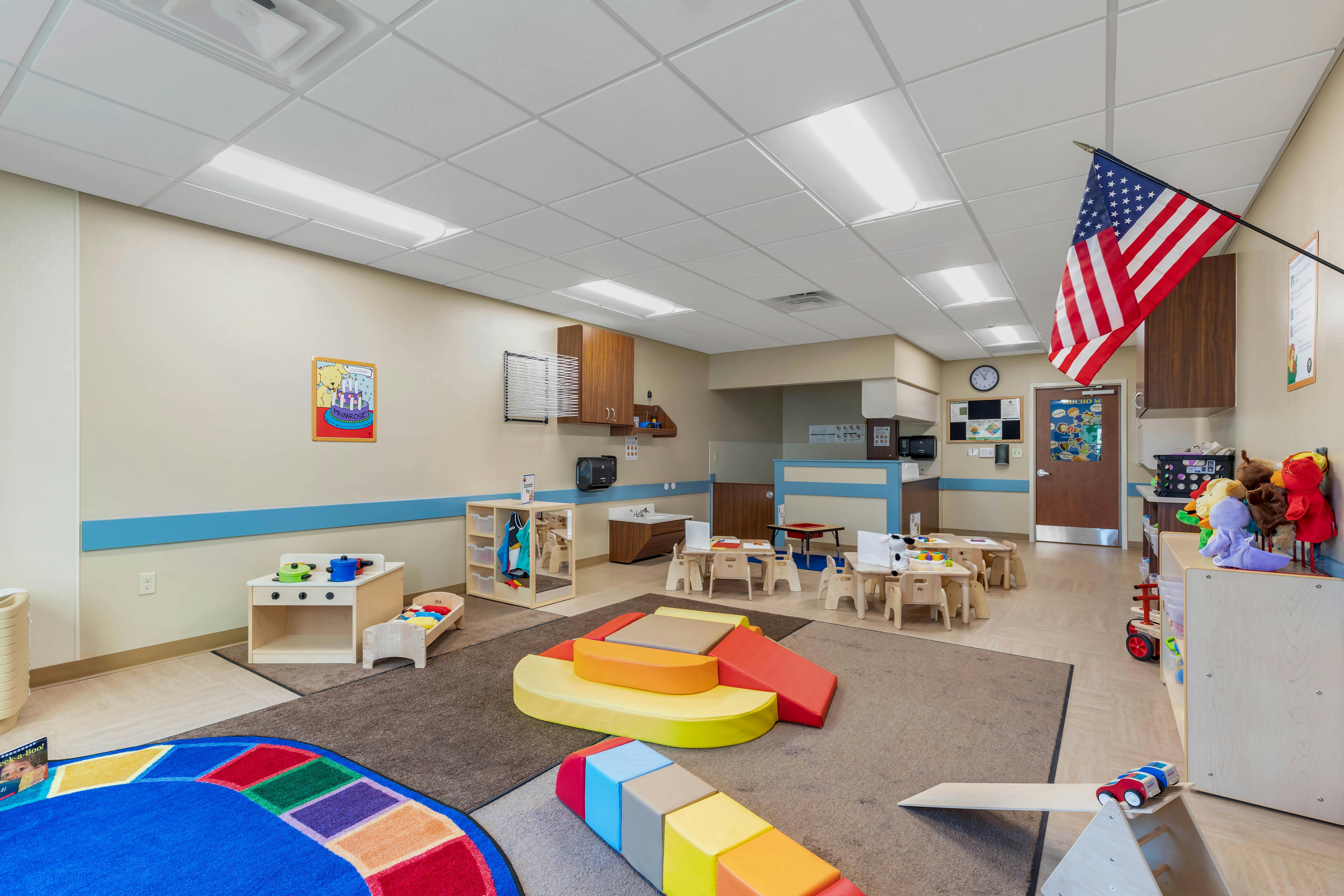 Classroom with small tables and chairs, play kitchen, colorful floor cushions