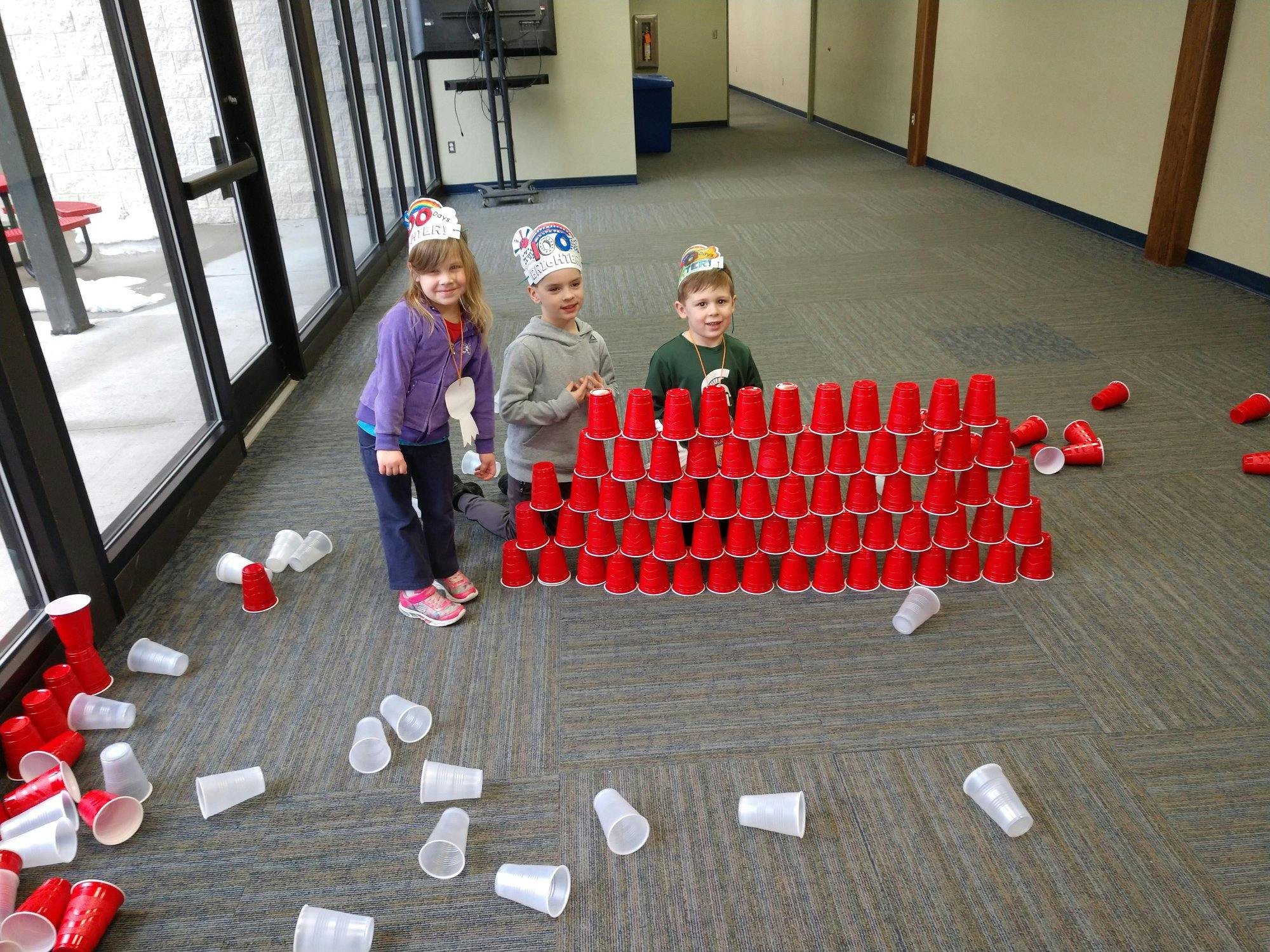 Three children standing behind a wall made of red plastic cups