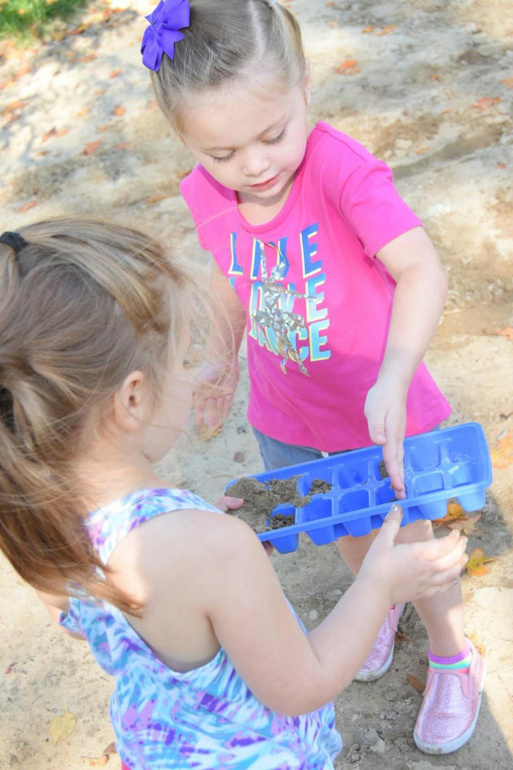 Two children playing with an ice cube tray filled with dirt