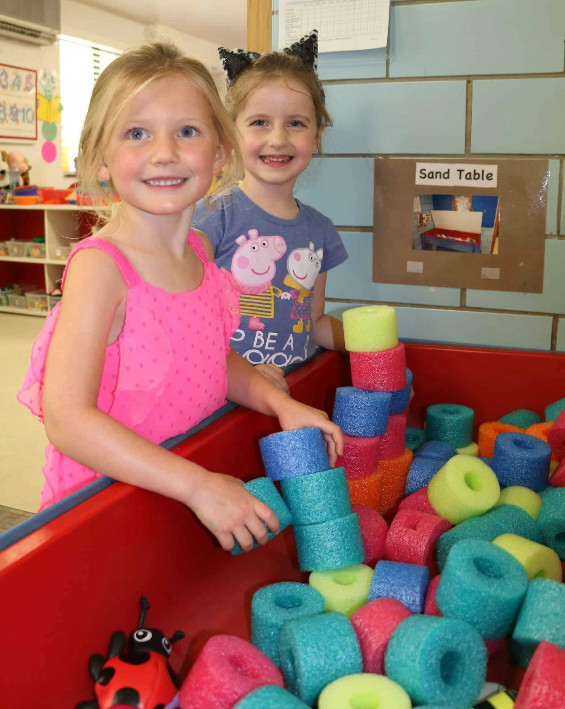 Two children playing with colorful foam rings in a red bin