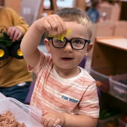 Child in glasses holding up a small yellow object