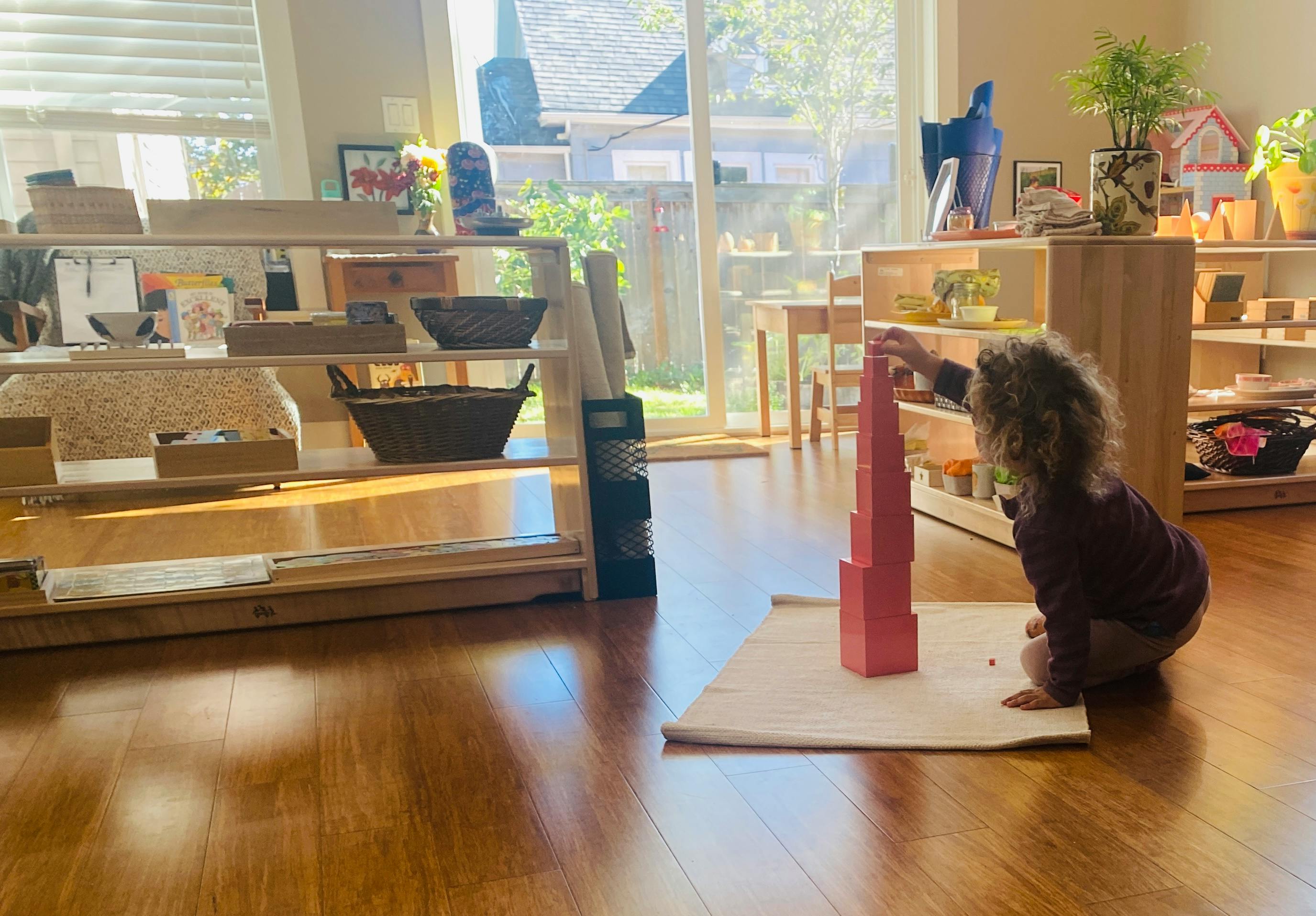 Child kneeling on floor building a tower with pink blocks in a classroom