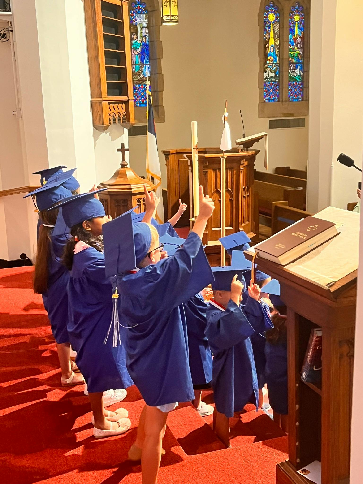 Children in graduation caps and gowns raising their hands in a church