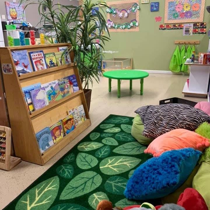 Bookshelf with children's books, green rug, and colorful pillows in a classroom