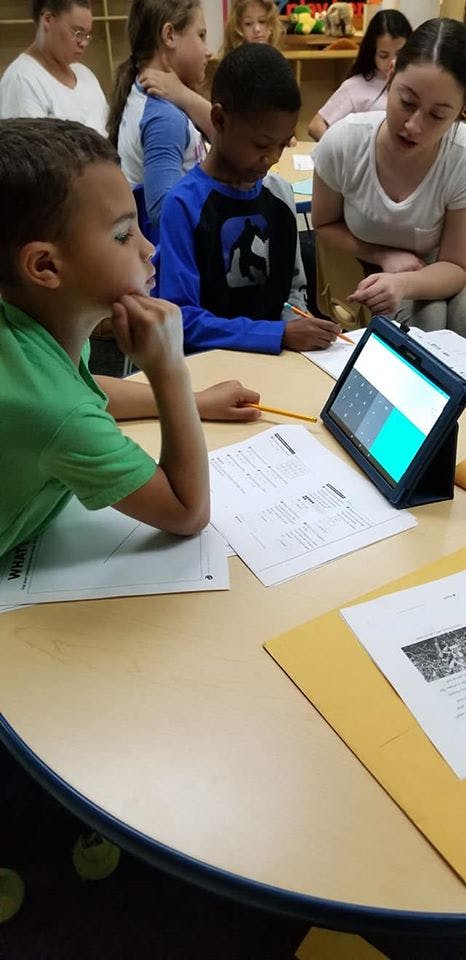 Children and adults at a table with a tablet and papers
