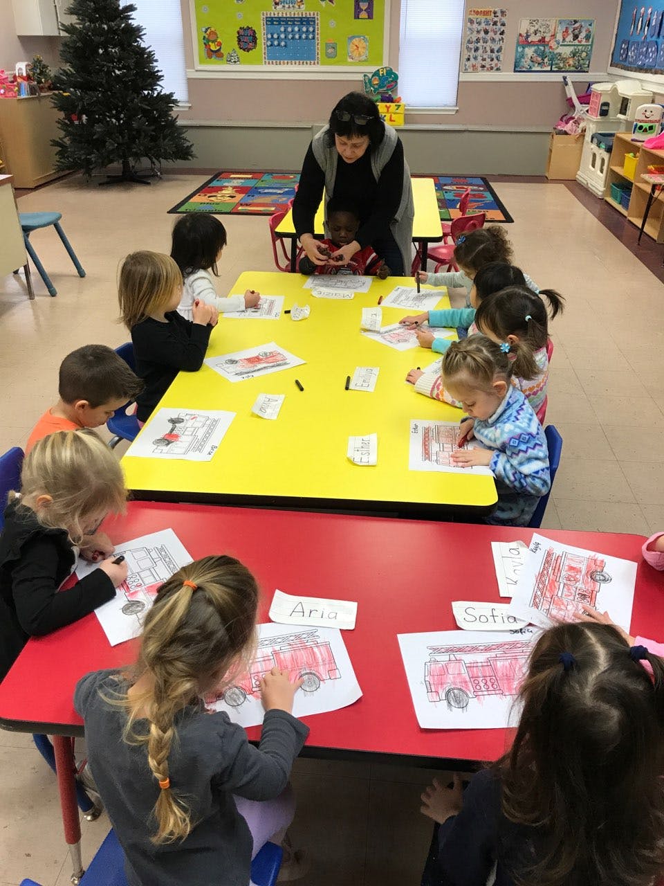 Adult and children coloring at tables in a classroom
