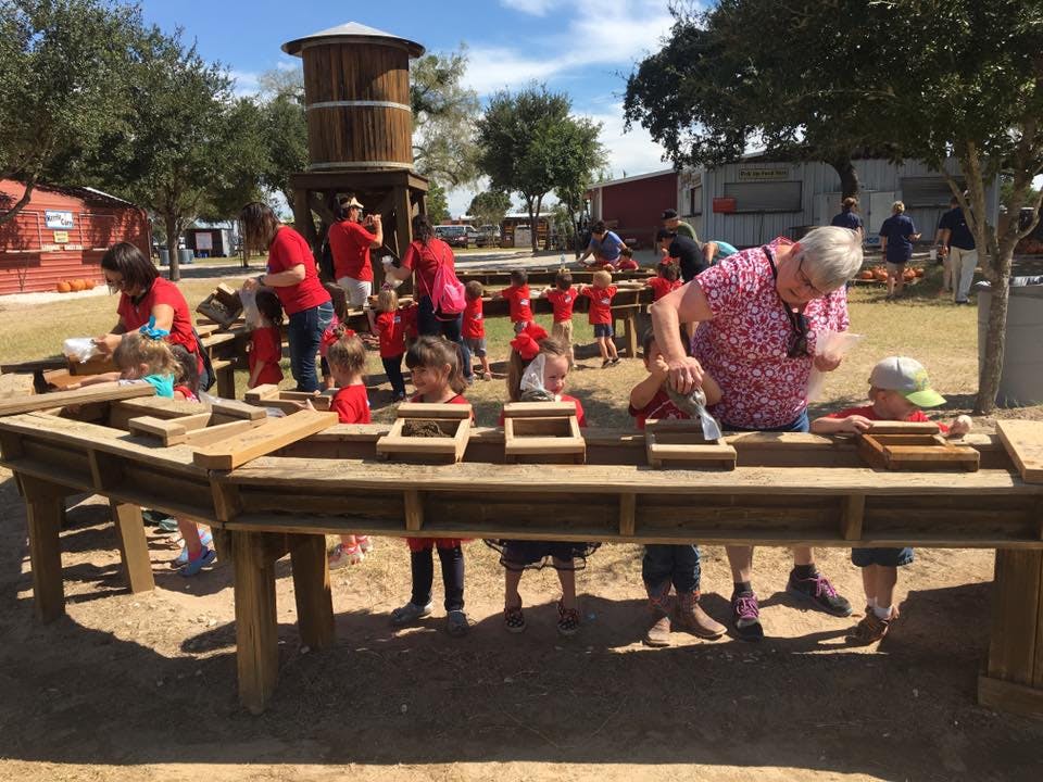 People and children panning for gold at wooden troughs