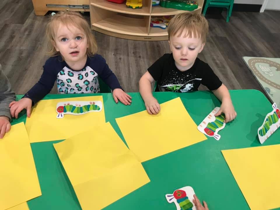 Two children at a table with yellow papers and caterpillar cutouts