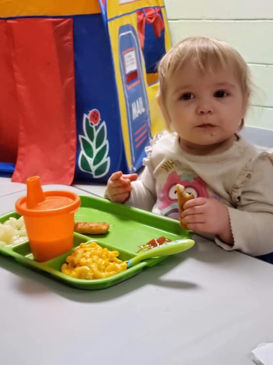 Child holding food with a meal tray in front