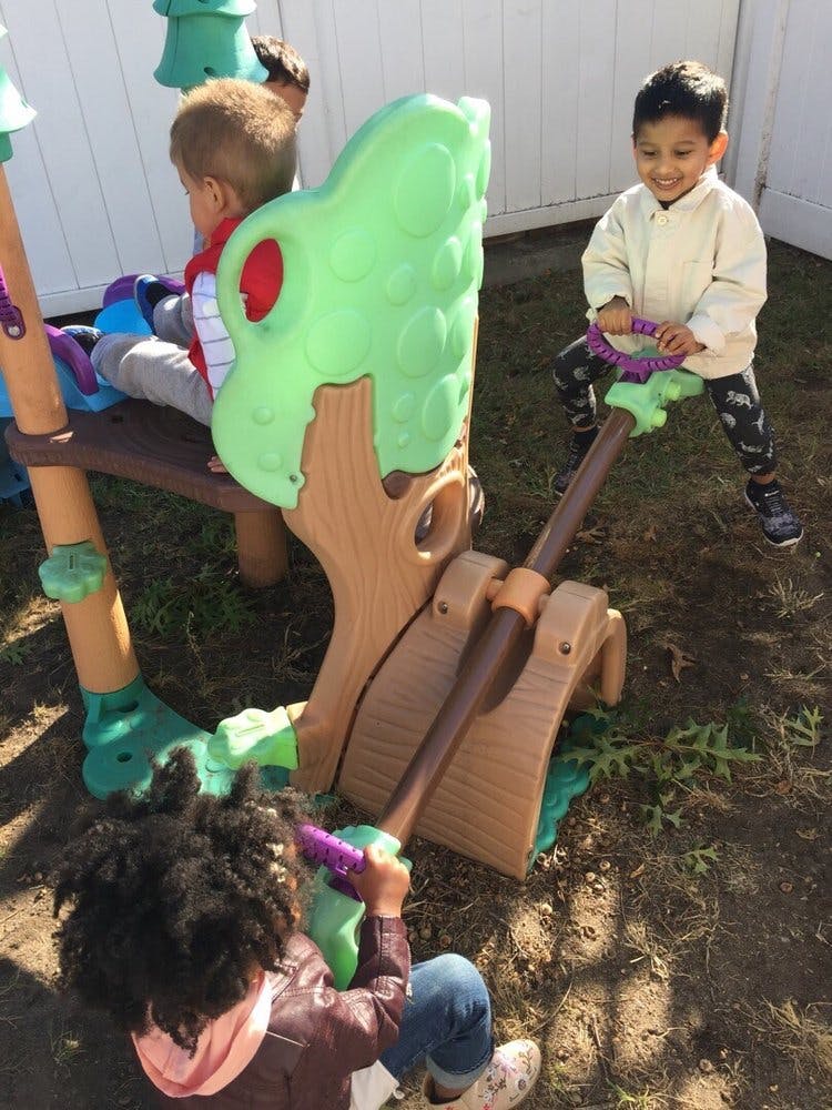 Three children playing on a seesaw and playground structure