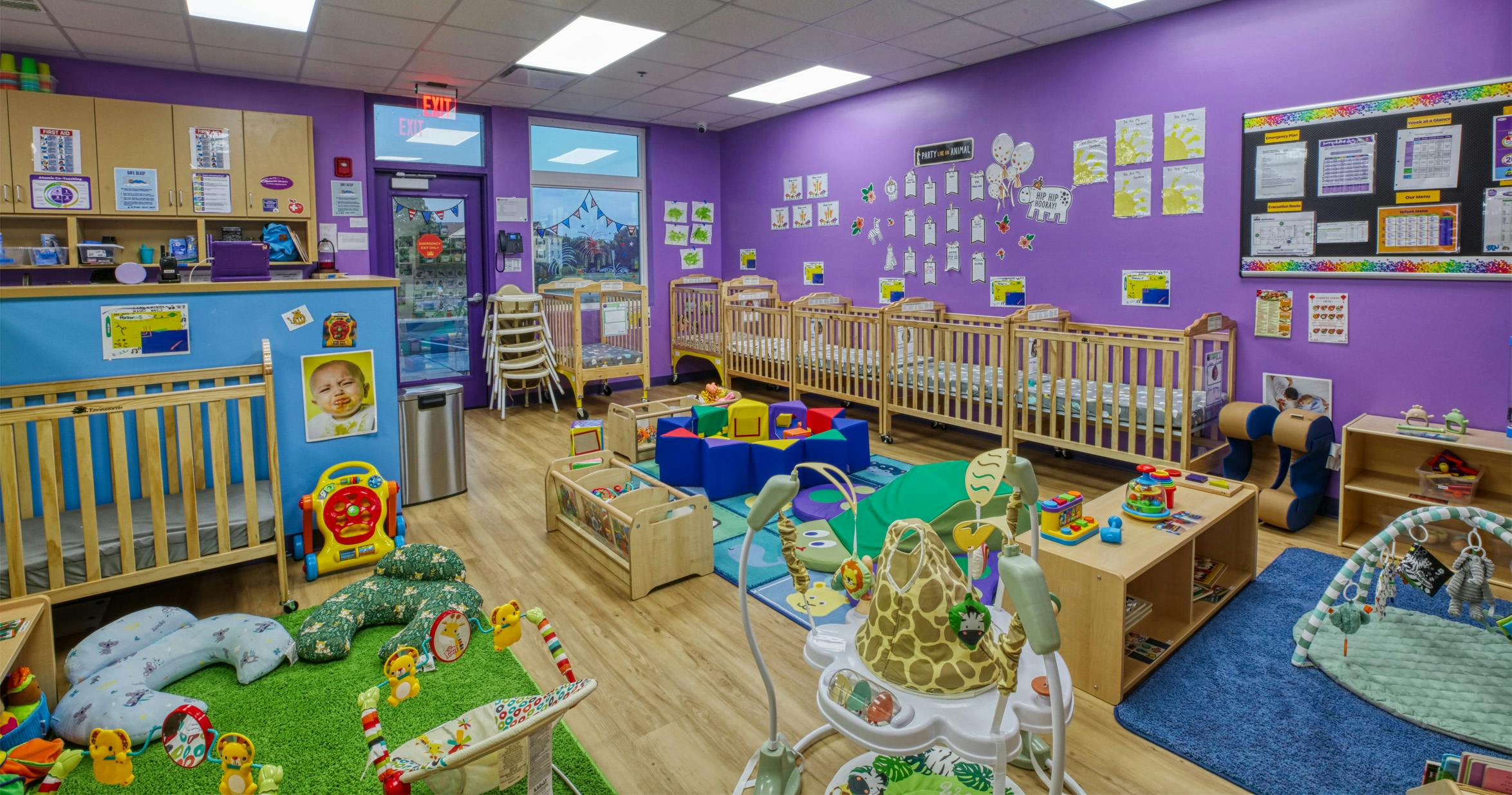 A colorful childcare room with cribs, play mats, and baby toys