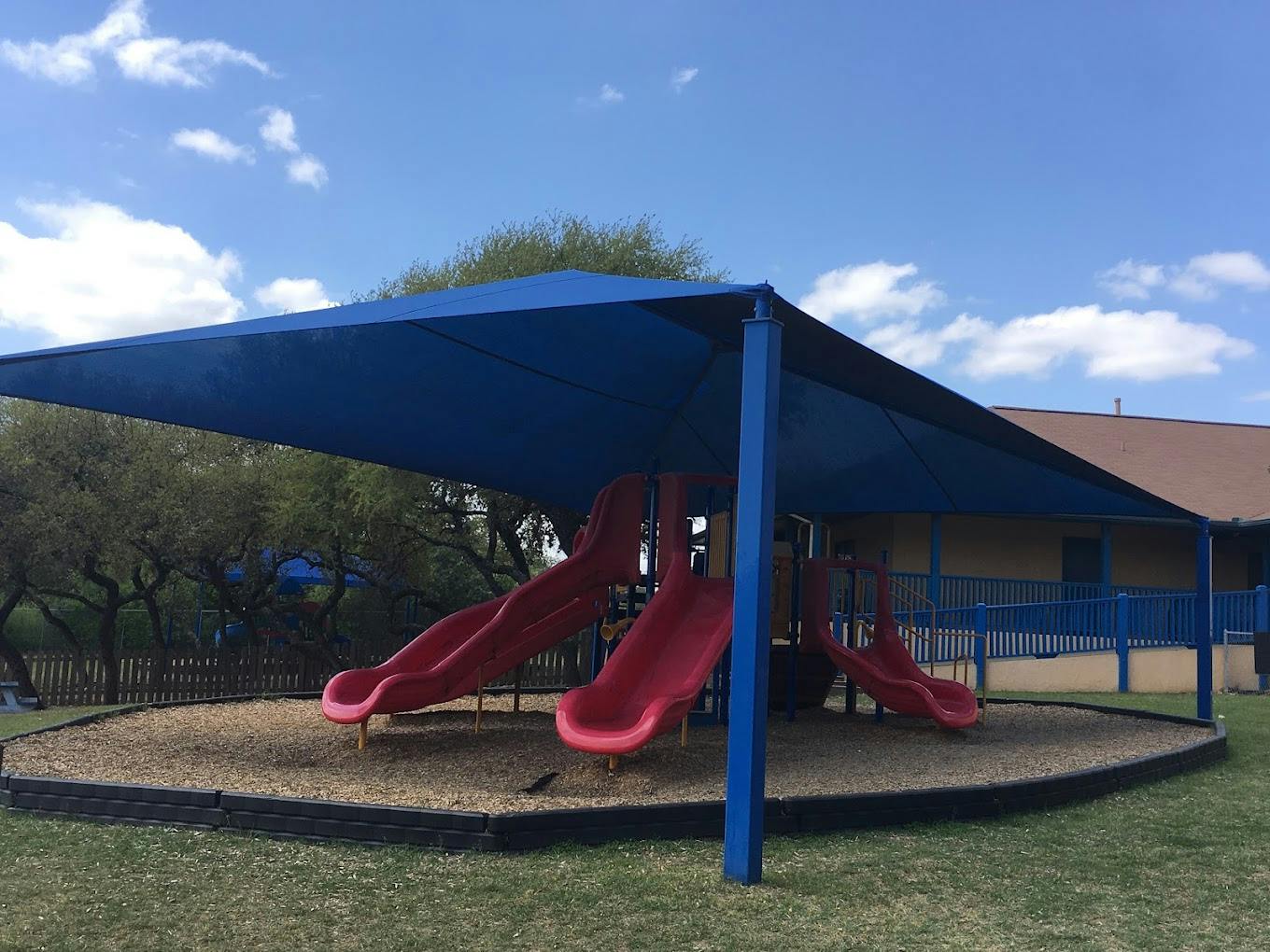 Playground equipment with red slides under a large blue shade canopy