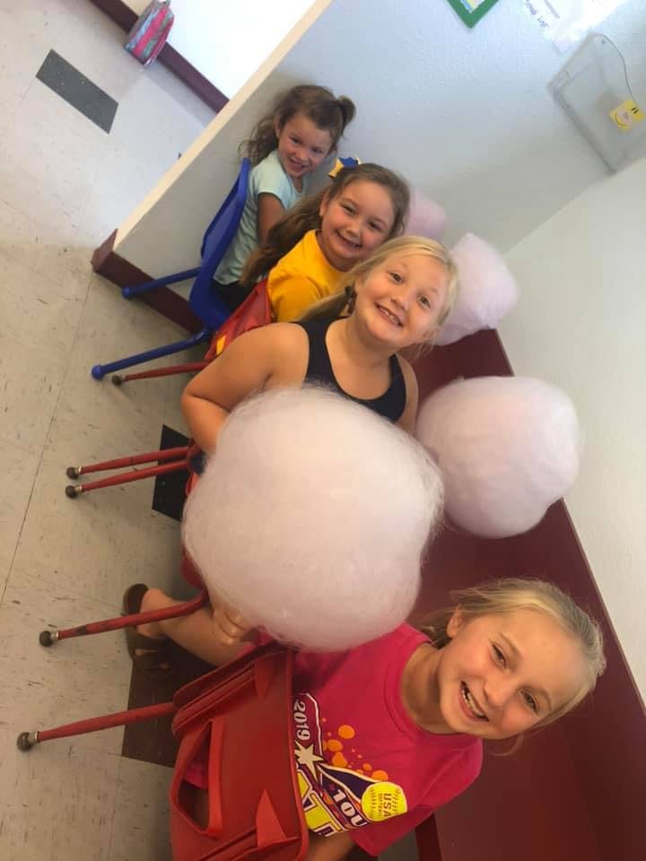 Four children sitting in chairs holding cotton candy