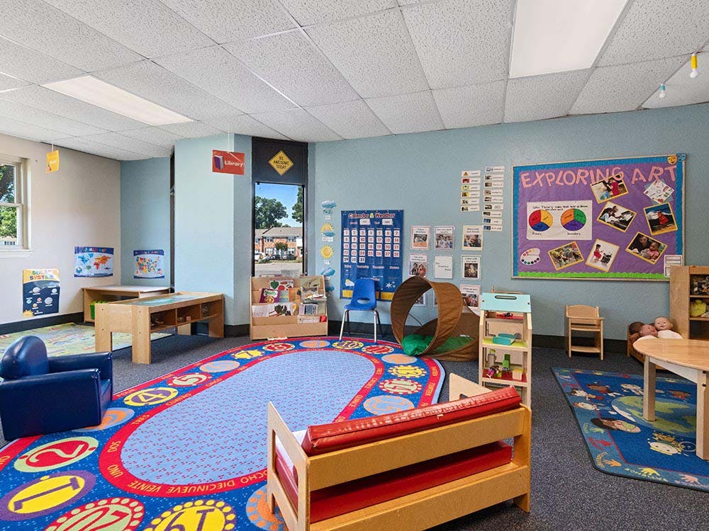 Classroom with a large colorful rug, small tables and chairs, and wall decorations