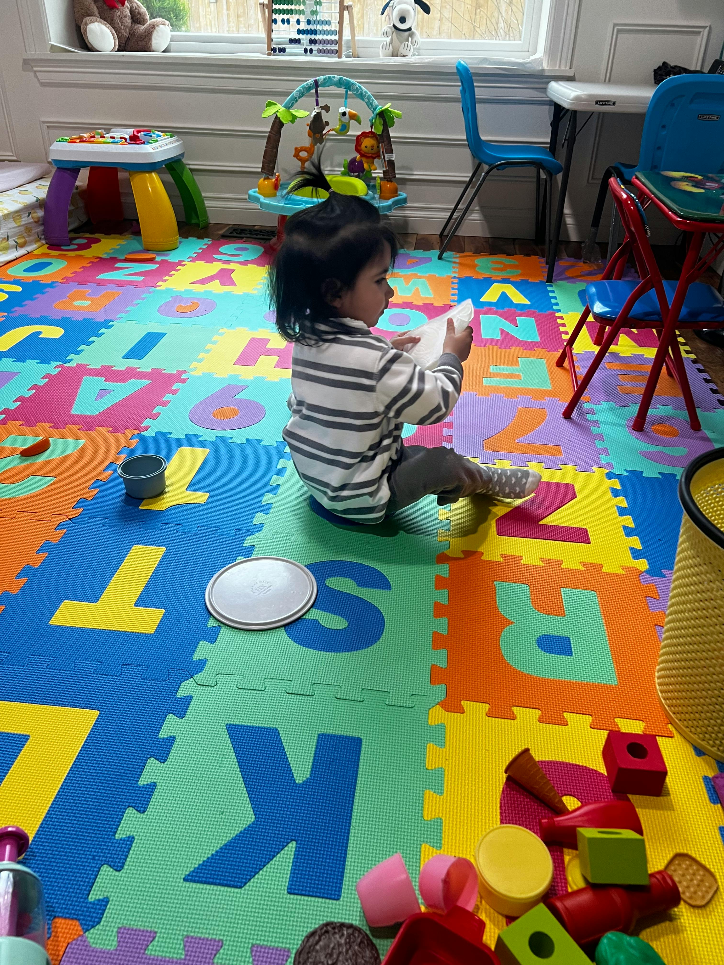 Child sitting on an alphabet playmat holding a small white object