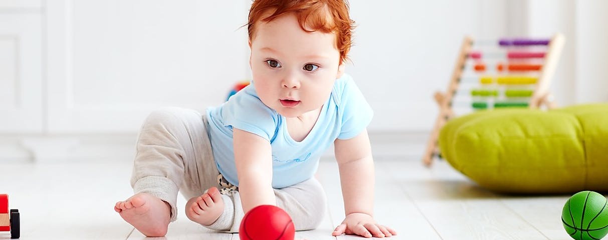 Child crawling on floor reaching for a red ball