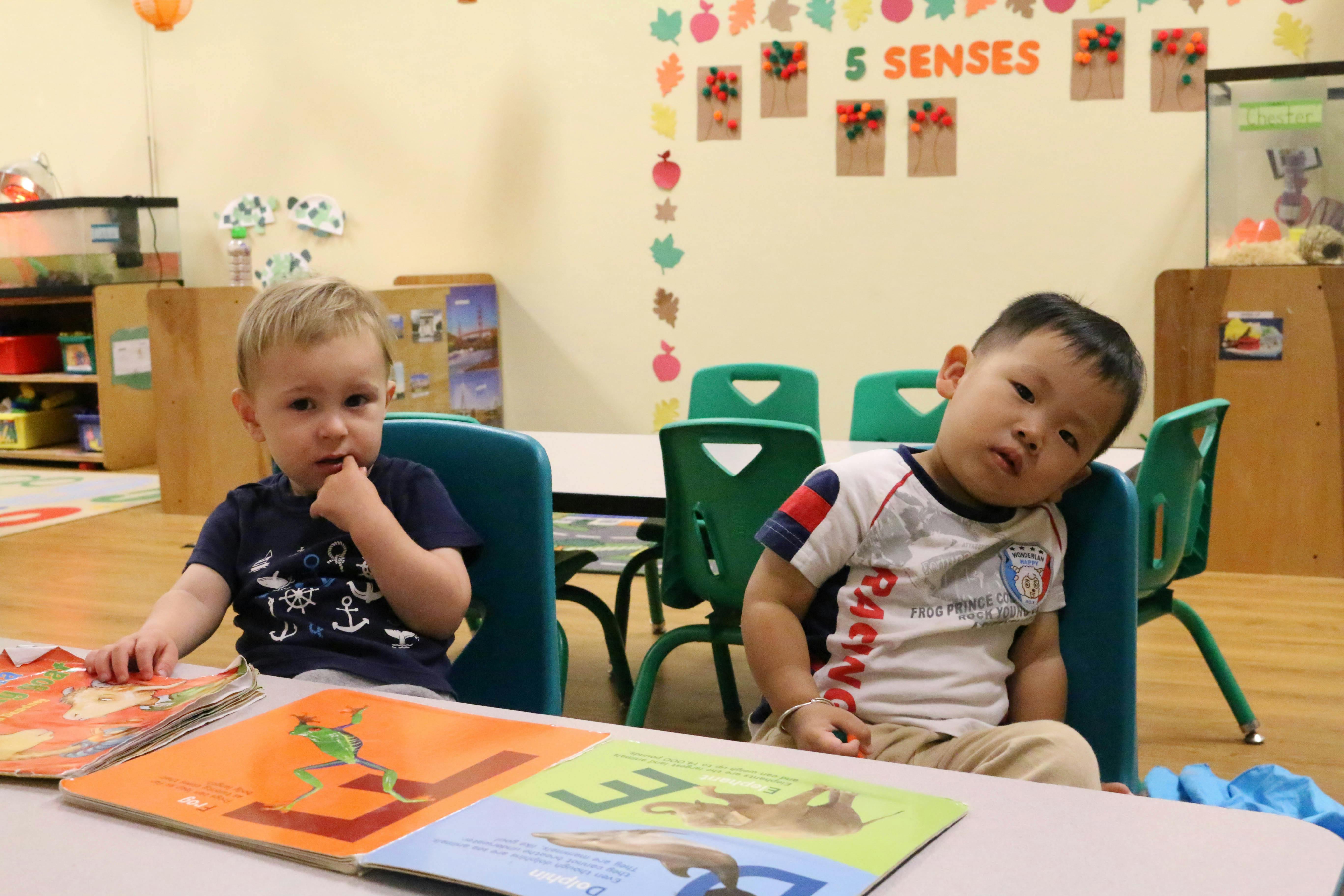 Two children sitting at a table with open books in a classroom