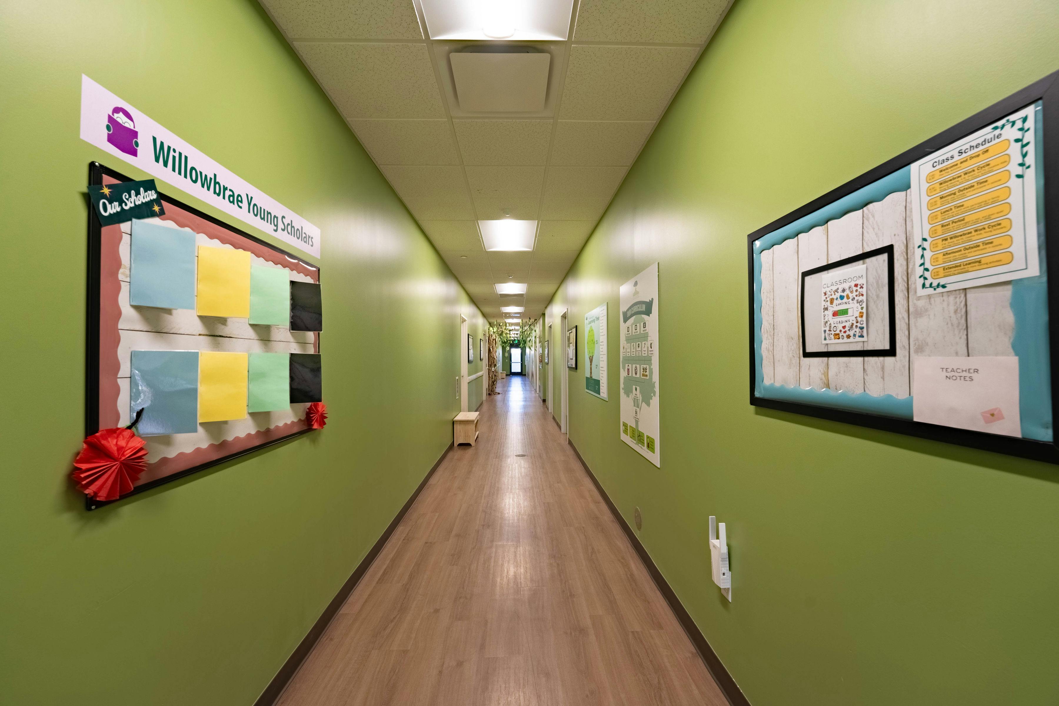 Long school hallway with green walls and bulletin boards displaying schedules and curriculum