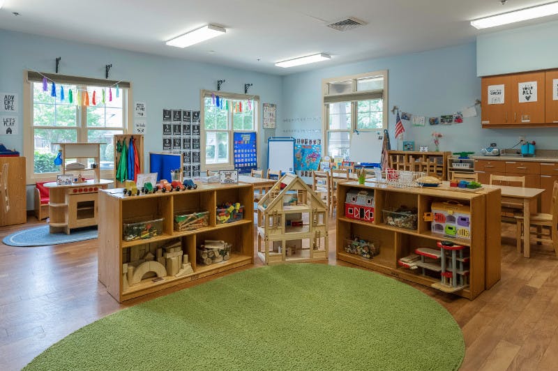Classroom with wooden shelves, toys, and a green circular rug