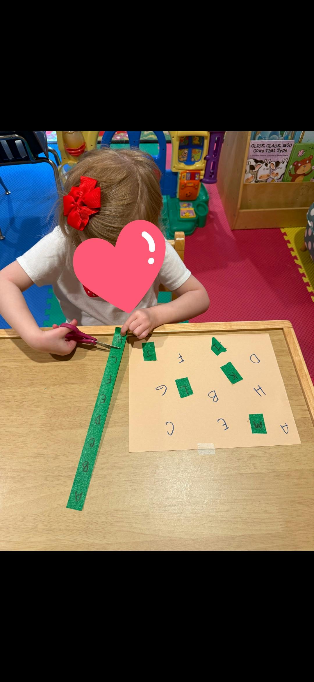 Child cutting a strip of green paper with letters on it