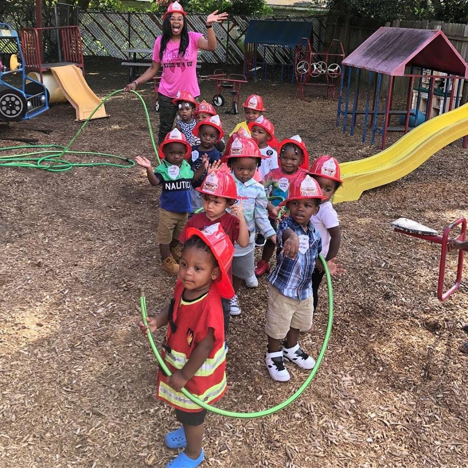 Adult and children in firefighter hats playing with a hose on a playground