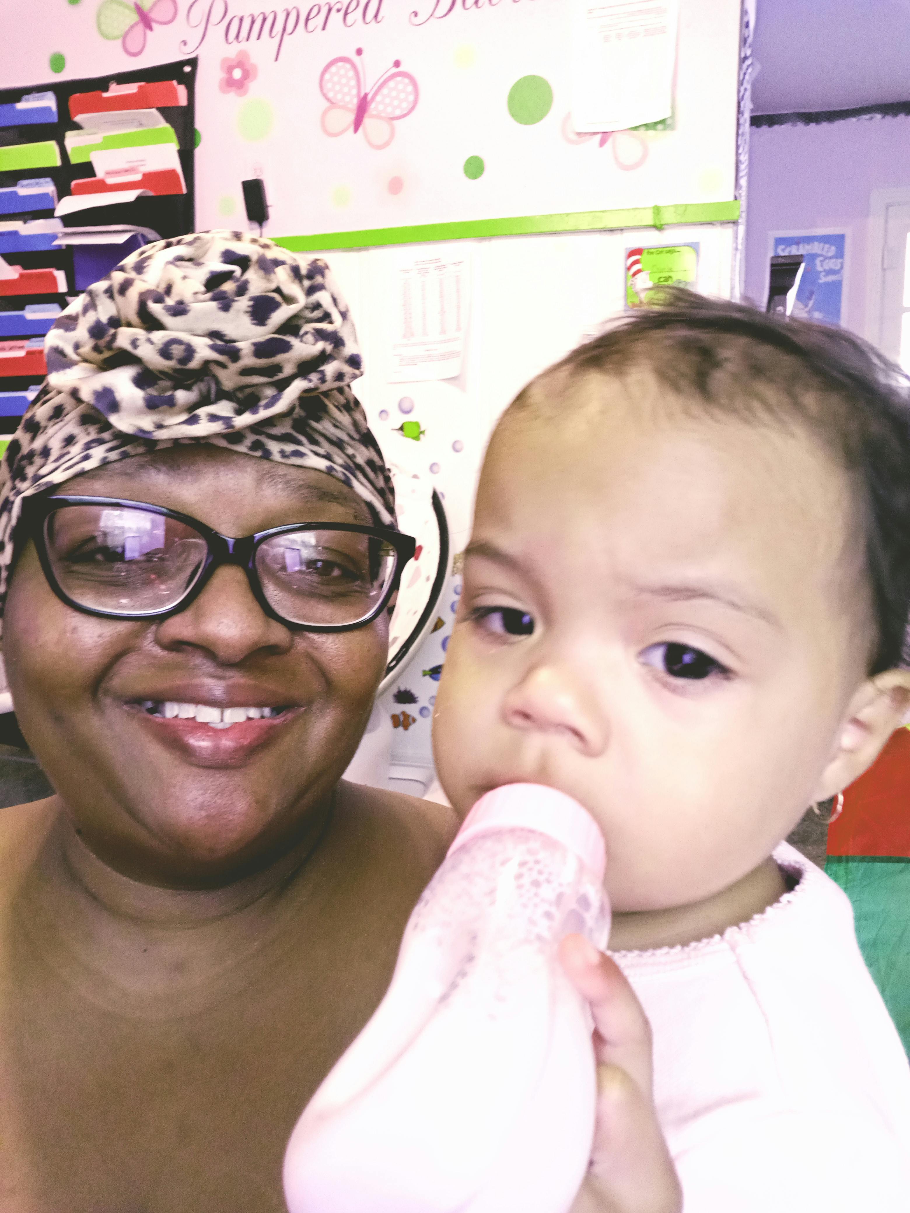 Person in glasses and head wrap with a child drinking from a bottle