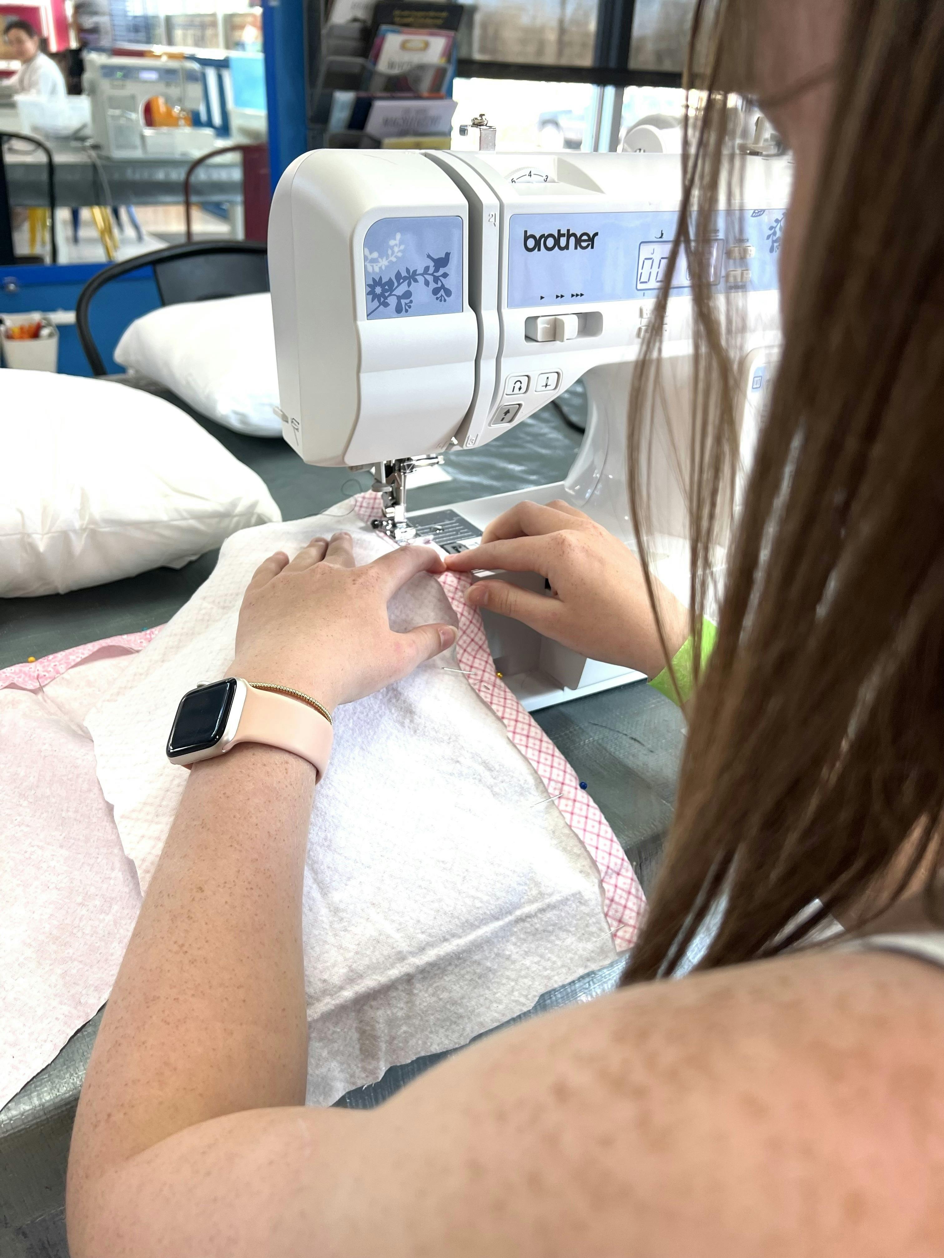 Person’s hands guiding fabric under a sewing machine needle