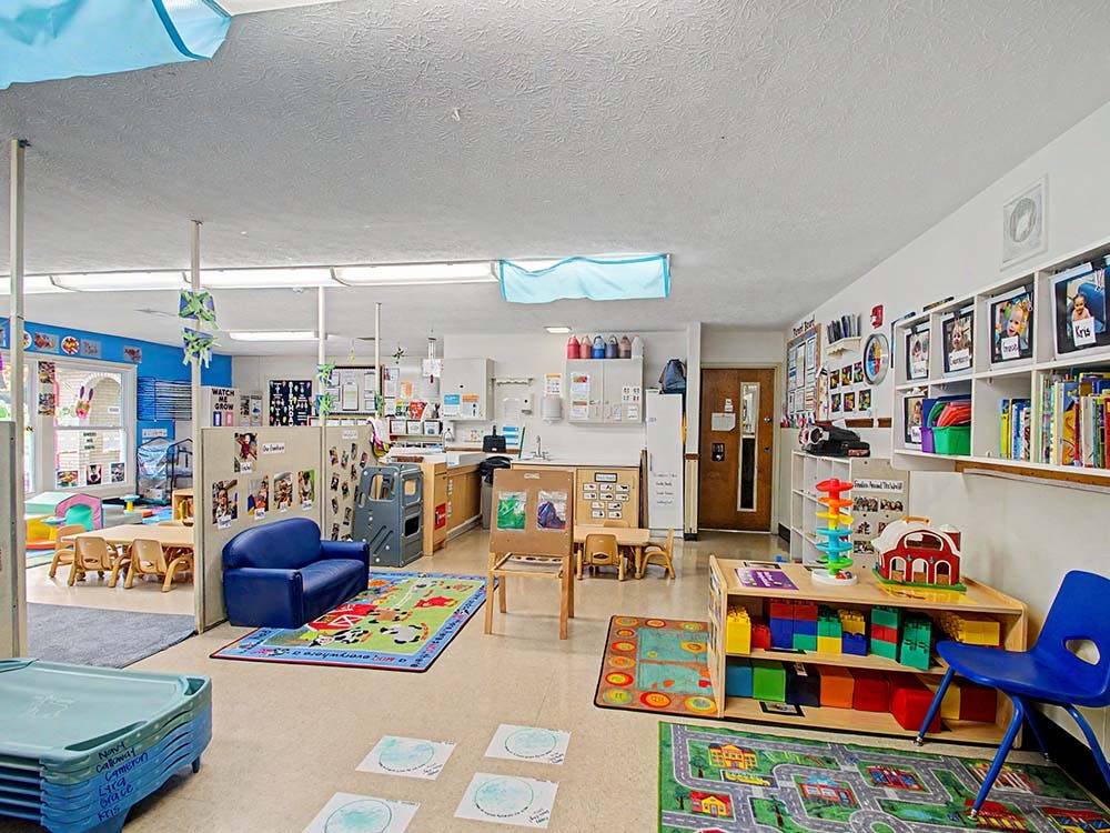 An empty daycare classroom with toys, rugs, and child-sized furniture