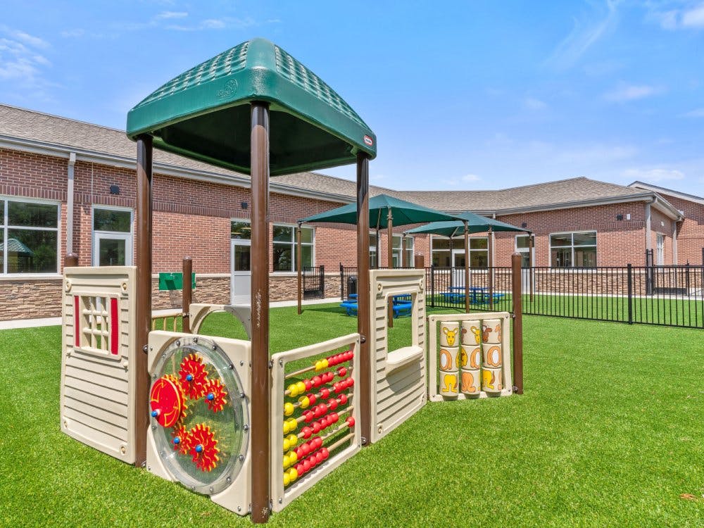 Playground equipment on green artificial turf outside a brick building