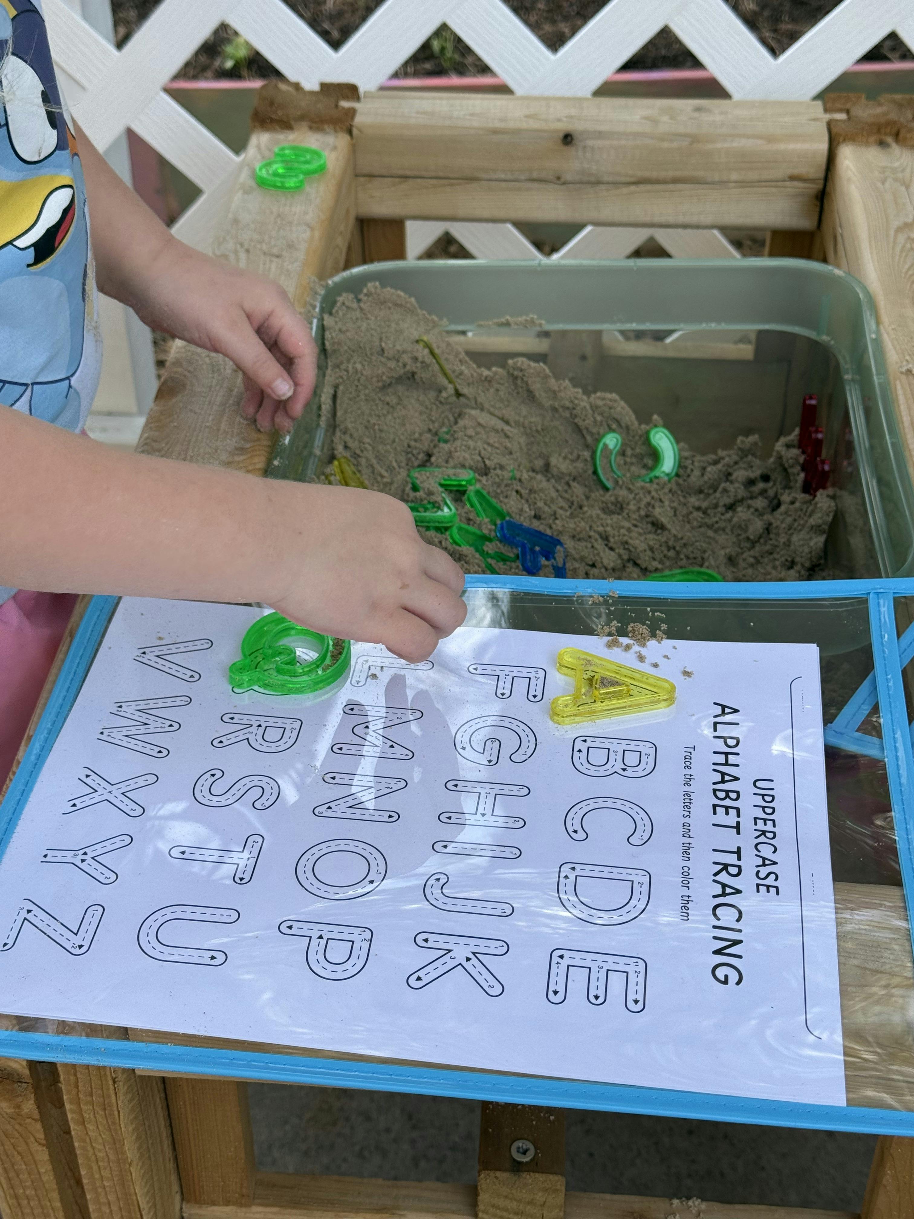 Child placing plastic letter shapes on an alphabet tracing worksheet