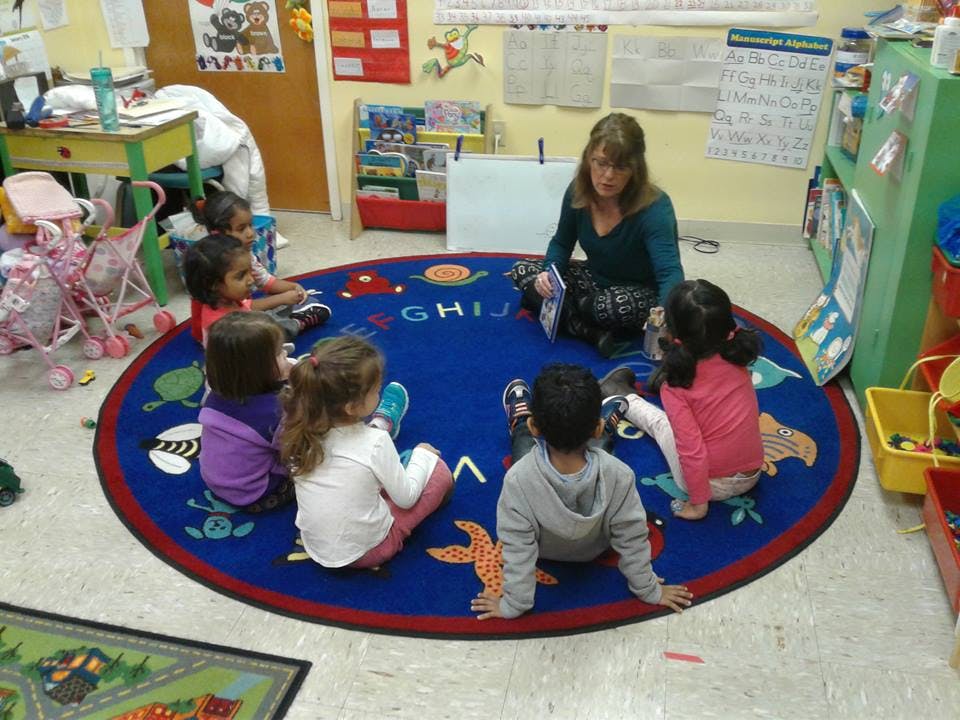 Adult and children sitting on a blue rug in a classroom