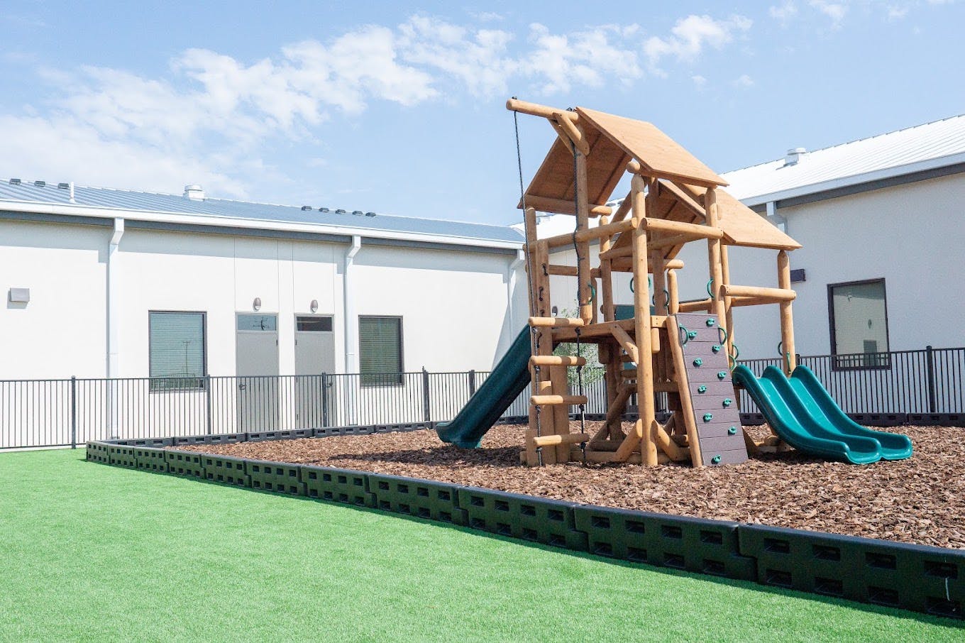 Wooden playground structure with slides in a fenced area