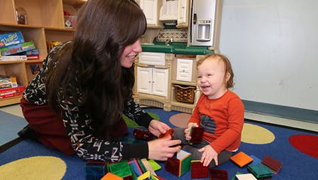 Person and child playing with colorful blocks on a rug