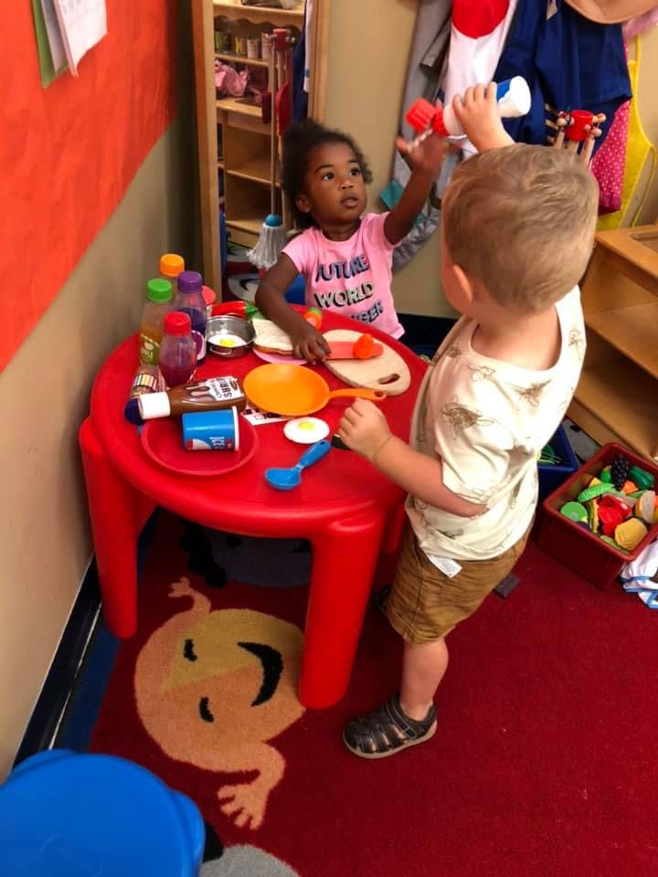 Two children playing with toy food at a red table