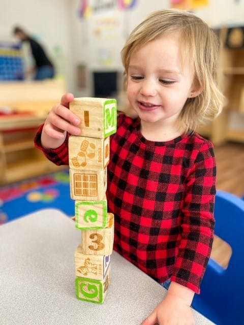 Child stacking wooden blocks with letters and numbers in a classroom