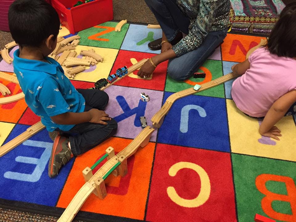 People playing with wooden tracks and small cars on an alphabet rug
