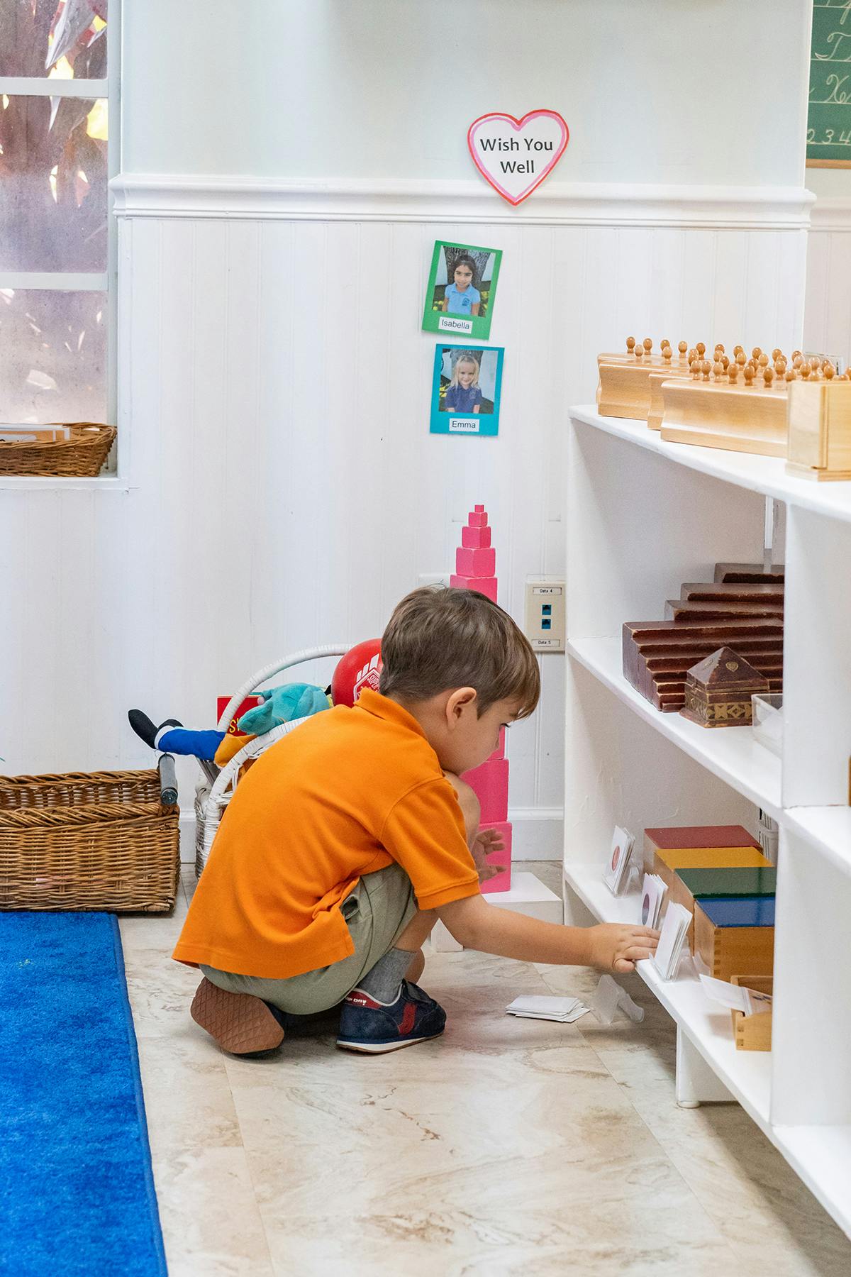 Child crouching and reaching for an item on a shelf in a classroom