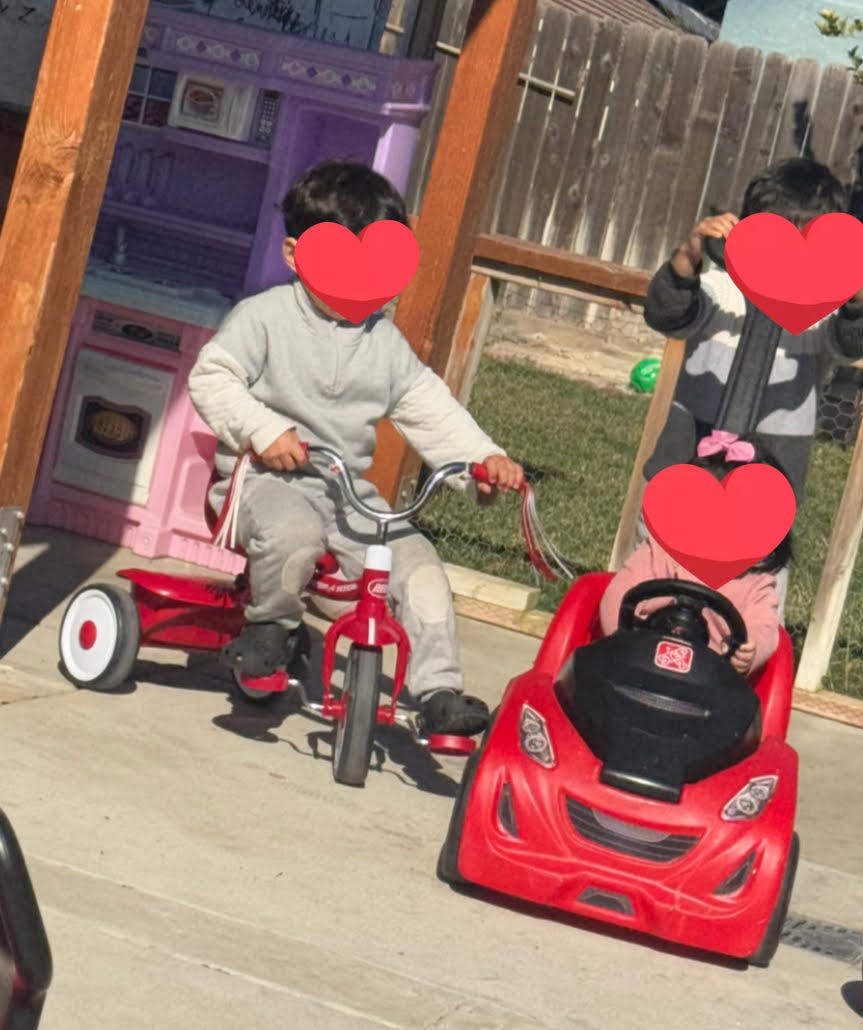 Child on a red tricycle next to another child in a red toy car