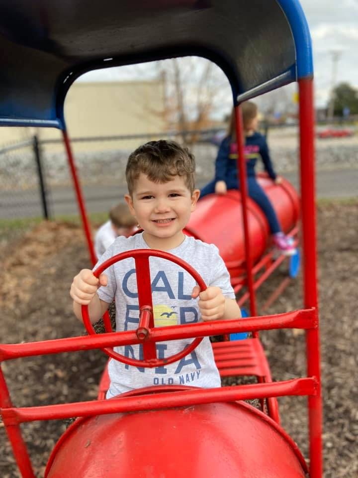 Child on a red playground structure holding a steering wheel