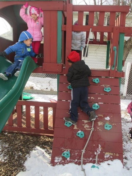Children playing on a wooden playground structure in the snow
