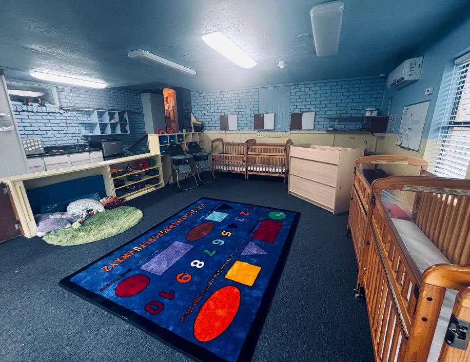 Childcare room with wooden cribs, high chairs, and an alphabet shape rug