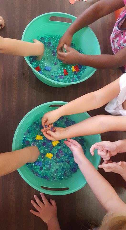 Children's hands playing with water beads and small toys in two green bins