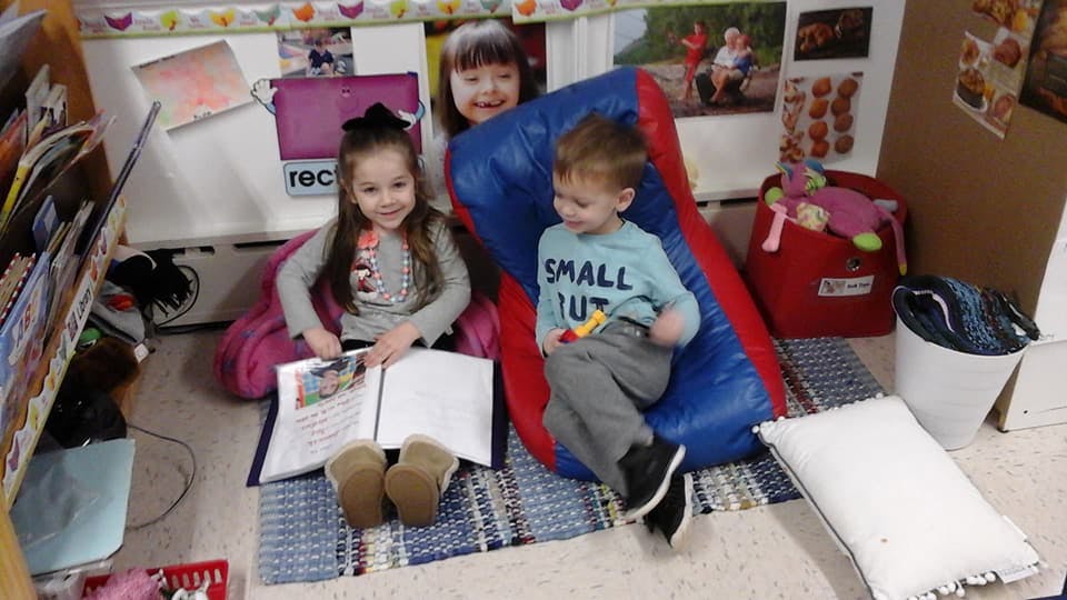 Two children sitting on the floor, one reading a book