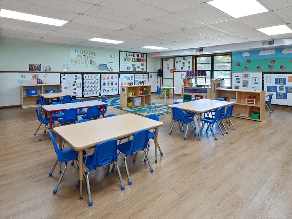 Empty preschool classroom with small tables and blue chairs